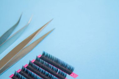 Güzellik ve moda kavramı - kirpik uzatma yordamı için araçlar. İki cımbız ile mavi arka plan üzerinde sahte kirpikleri. boşaltmak mockup