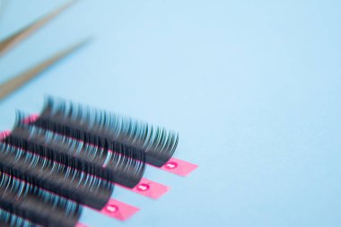 Güzellik ve moda kavramı - kirpik uzatma yordamı için araçlar. İki cımbız ile mavi arka plan üzerinde sahte kirpikleri. boşaltmak mockup