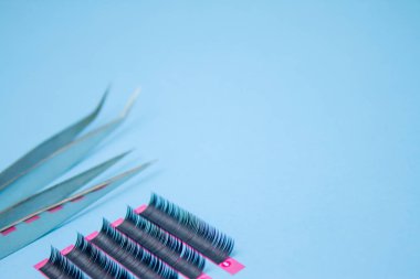 Güzellik ve moda kavramı - kirpik uzatma yordamı için araçlar. İki cımbız ile mavi arka plan üzerinde sahte kirpikleri. boşaltmak mockup