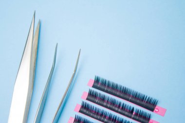 Güzellik ve moda kavramı - kirpik uzatma yordamı için araçlar. İki cımbız ile mavi arka plan üzerinde sahte kirpikleri. boşaltmak mockup