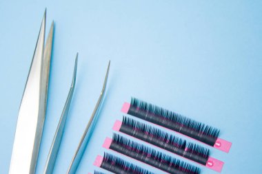 Güzellik ve moda kavramı - kirpik uzatma yordamı için araçlar. İki cımbız ile mavi arka plan üzerinde sahte kirpikleri. boşaltmak mockup