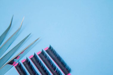 Güzellik ve moda kavramı - kirpik uzatma yordamı için araçlar. İki cımbız ile mavi arka plan üzerinde sahte kirpikleri. boşaltmak mockup