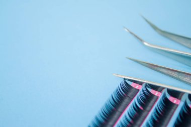 Güzellik ve moda kavramı - kirpik uzatma yordamı için araçlar. İki cımbız ile mavi arka plan üzerinde yapay siyah kırbaç. boşaltmak mockup