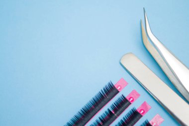 Güzellik ve moda kavramı - kirpik uzatma yordamı için araçlar. İki cımbız ile mavi arka plan üzerinde yapay siyah kırbaç. boşaltmak mockup