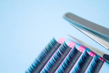 Güzellik ve moda kavramı - kirpik uzatma yordamı için araçlar. İki cımbız ile mavi arka plan üzerinde yapay siyah kırbaç. boşaltmak mockup