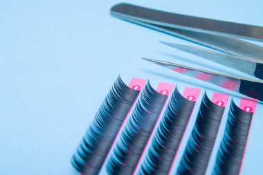 Beauty and fashion concept - tools for Eyelash Extension Procedure. Two tweezers with artificial black lashes on blue background. copyspace mockup clipart