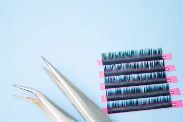 Beauty and fashion concept - tools for Eyelash Extension Procedure. Two tweezers with false lashes on blue background. copyspace mockup