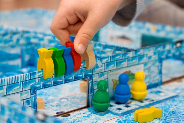 Board game and kids leisure concept - little boy hold red yellow, blue, green wood chips figure in hand in children play