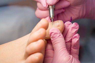 Profesyonel donanım pedikür pembe eldiven ve elektrikli cihaz makine kullanarak. Hastaya tıbbi pedikür yordamı, ayak hastalıkları uzmanı ziyaret etti. Peeling Ayak. Ayak tedavi Spa salonda. Podiatry Kliniği