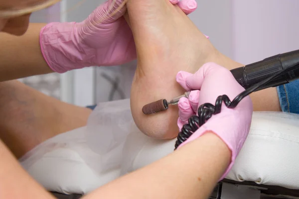 Professional hardware pedicure using pink gloves and electric device machine. Patient on medical pedicure procedure, visiting podiatrist. Peeling feet. Foot treatment in SPA salon.Podiatry clinic