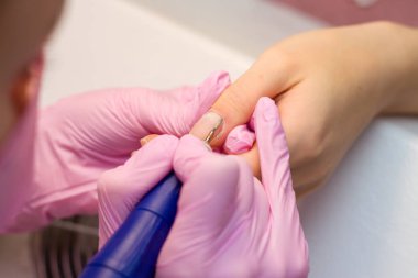 Elektrikli cihaz makine kullanarak donanım manikür. tırnak cilası uygulamadan önce çivi hazırlanması için yordam. Elinde manikürcü pembe eldiven ve istemci çivi. Kadın güzellik salonu.