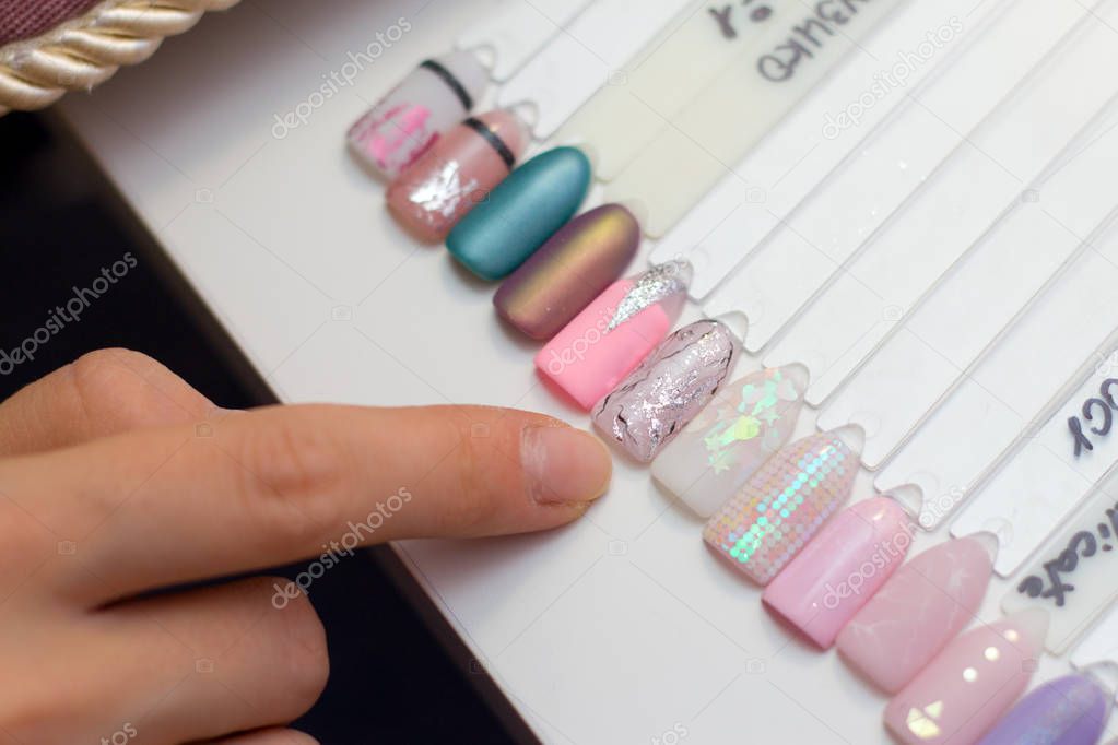 Manicure and nail care concept. A woman in a beauty salon holds colored test nail polishes with different colors and chooses the color for painting.