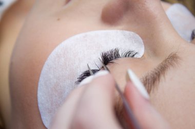 Kirpik uzatma yordamı. Kadın uzun yanlış Eyelashes gözle. Beautican bir elinde cımbız makro çekim kapatın