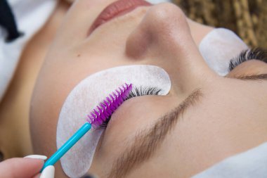 Kirpik uzatma yordamı. Kadın uzun yanlış Eyelashes gözle. Beautican bir elinde cımbız makro çekim kapatın