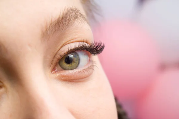 Eyelash Extension Procedure. Woman Eye with Long false Eyelashes. Close up macro shot of fashion eyes visagein in beauty salon.