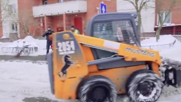 2019年2月8日 俄罗斯圣彼得堡 服务公司从冰雪中清理房子的院子和人行道 山猫或滑行装载机的雪移小拖拉机用水桶清理道路 — 图库视频影像