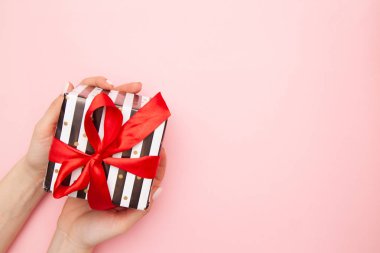 kadın elleriyle hediye kutusunda siyah ve beyaz çizgili pembe masa üstü görünümü üzerinde izole kırmızı şerit yay ile mevcut. En az düz kompozisyon satışlar, doğum günü, anneler günü ya da Noel için yatıyordu. boşaltmak