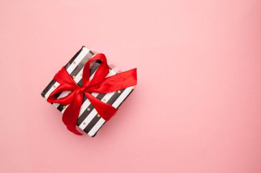 Hediye veya siyah ve beyaz çizgili pembe tablo üstten görünüm üzerinde izole kırmızı şerit yay ile mevcut kutusunda. En az düz kompozisyon satışlar, doğum günü, anneler günü ya da Noel için yatıyordu. boşaltmak