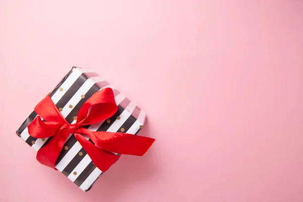 Gift or present box in white and black stripes with a red ribbon bow isolated on pink table top view. Minimal flat lay composition for sales, birthday, mother day or christmas. copyspace — Stock Photo, Image