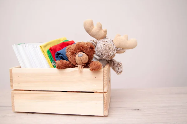 Donation concept. Donate box with kids clothes, books, school supplies and toys. Teddy bear and moose toy. Copyspace for text.