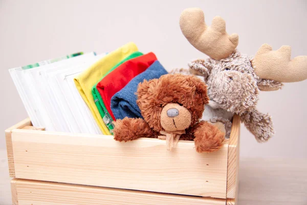 Donation concept. Donate box with kids clothes, books, school supplies and toys. Teddy bear and moose toy.