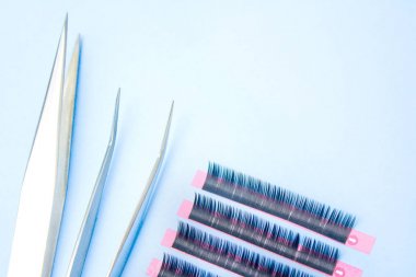 Kirpik uzatma prosedürü için araçlar. Mavi arka planda yanlış kirpiklere sahip iki cımbız. boşaltmak mockup-güzellik ve moda konsepti