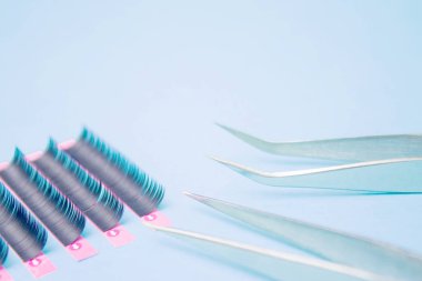Kirpik uzatma prosedürü için araçlar. Mavi arka planda yanlış kirpiklere sahip iki cımbız. boşaltmak mockup-güzellik ve moda konsepti