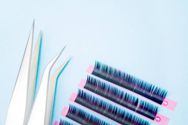 Kirpik uzatma prosedürü için araçlar. Mavi arka planda yapay siyah kirpiklere sahip iki cımbız. boşaltmak mockup-güzellik ve moda konsepti