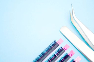 Kirpik uzatma prosedürü için araçlar. Mavi arka planda yapay siyah kirpiklere sahip iki cımbız. boşaltmak mockup-güzellik ve moda konsepti