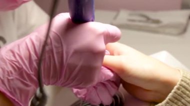 Elektrikli cihaz makine kullanarak donanım manikür. tırnak cilası uygulamadan önce çivi hazırlanması için yordam. Elinde manikürcü pembe eldiven ve istemci çivi. Kadın güzellik salonu.