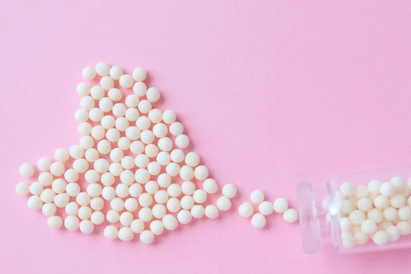 Heart made of homeopathic globules and glass bottle on pink background. Alternative Homeopathy medicine herbs, healtcare and pills concept. Flatlay. Top view. copyspace for text
