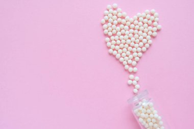 Kalp pembe arka plan üzerinde homeopatik globüller ve cam şişe yapılmış. Alternatif Homeopati ilaç otlar, şifalı bakım ve hap kavramı. Düzlay. Üst te. metin için copyspace