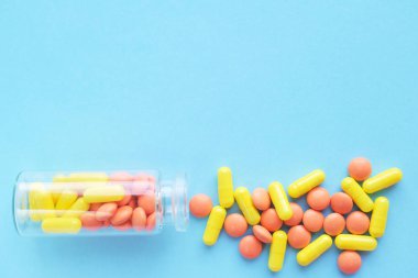 Mavi arka plan üzerinde cam şişe sarı ve turuncu kapsüller. metin için copyspace. Salgın, ağrı kesiciler, sağlık, tedavi hapları ve uyuşturucu bağımlılığı kavramı