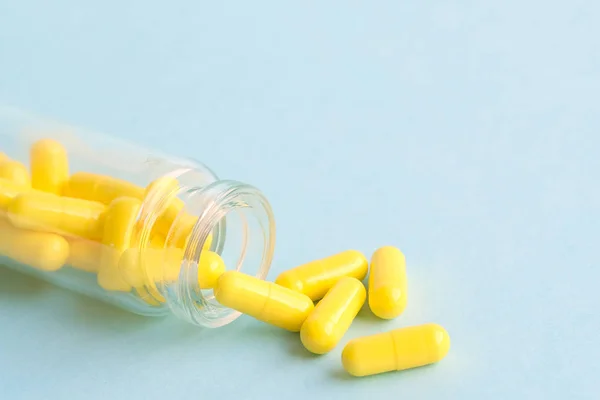 Žluté tobolky ze skleněné lahvičky na modrém pozadí. copyspace pro text. Epidemie, léky proti bolesti, zdravotní péče, léčebné pilulky a koncepce užívání drog — Stock fotografie