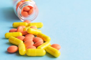 Mavi arka plan üzerinde cam şişe sarı ve turuncu kapsüller. metin için copyspace. Salgın, ağrı kesiciler, sağlık, tedavi hapları ve uyuşturucu bağımlılığı kavramı