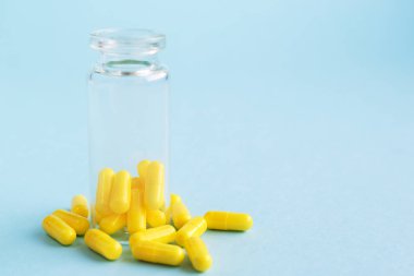 Mavi arka plandaki cam şişeden sarı kapsüller. metin için metin boşluğu. Salgın, ağrı kesiciler, sağlık hizmetleri, tedavi hapları ve uyuşturucu bağımlılığı kavramı