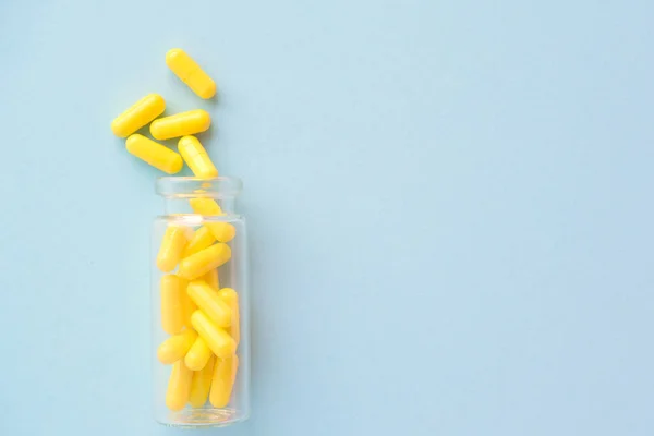 Žluté tobolky ze skleněné lahvičky na modrém pozadí. copyspace pro text. Epidemie, léky proti bolesti, zdravotní péče, léčebné pilulky a koncepce užívání drog — Stock fotografie