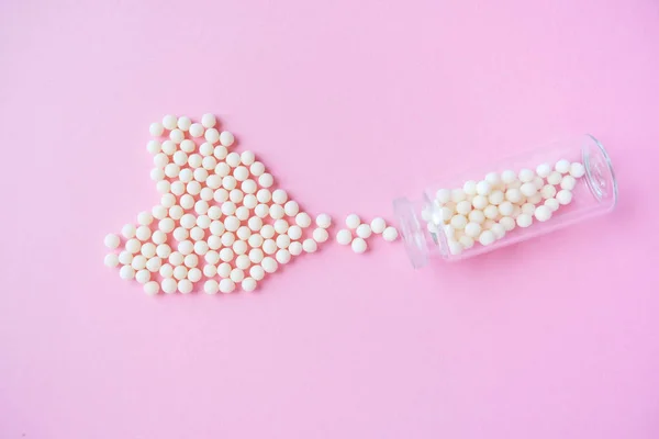 Heart made of homeopathic globules and glass bottle on pink background. Alternative Homeopathy medicine herbs, healtcare and pills concept. Flatlay. Top view. copyspace for text