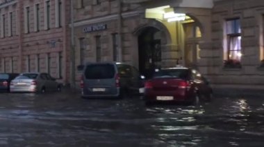 Sular altında kalan şehir caddesinde büyük su sıçrayan araba trafiği. Geceleri asfalt yolda büyük su birikintisi. Acil durum - su kanalizasyonları şiddetli yağmurla başa çıkamaz, tufan 26 haziran 2019 St.Petersburg Rusya