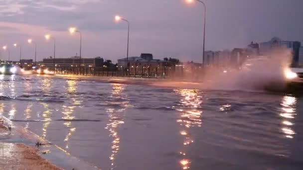 浸水した市街地の通りに大きな飛沫を持つ車のトラフィック 夜のアスファルト道路の大きな水たまり 雨の後の道 水の排水管は 豪雨に対処することはできません — ストック動画