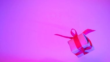 Neon mor arka plan üzerinde dönen kırmızı kurdele ile Hediye kutusu. 360 derece dönüş. sorunsuz döngü. sıfır yerçekimi. Levitation. copyspace. Konsept satış, indirimli fiyat, noel tatilleri ve alışveriş.