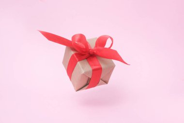 Pembe arka planda kırmızı kurdele ile hediye kutusu. sıfır yerçekimi. Levitation. milimalizm. Konsept satış, alışveriş, yılbaşı tatili ve Doğum günü