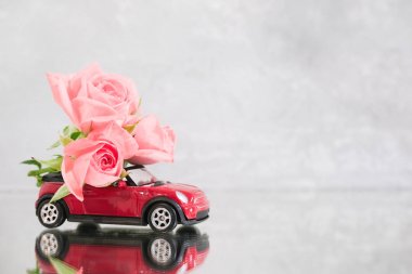 Gri arka plan üzerinde pembe gül çiçekleri buketteslim Kırmızı oyuncak araba. Ayna yansıması. Metin için yer. 14 Şubat kartı, Sevgililer Günü. Çiçek teslimatı. 8 Mart, Dünya Mutlu Kadınlar Günü.