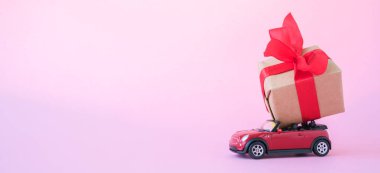 Kırmızı oyuncak araba pembe arka plan üzerinde kırmızı kurdele ile hediye kutusu teslim banner. Metin için yer. Satış, Doğum Günü, Noel zamanı