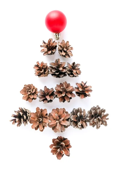 Layout creativo dell'albero di Natale fatto di coni di abete e palla rossa su sfondo bianco. Piatto. Natura concetto di Capodanno . — Foto Stock