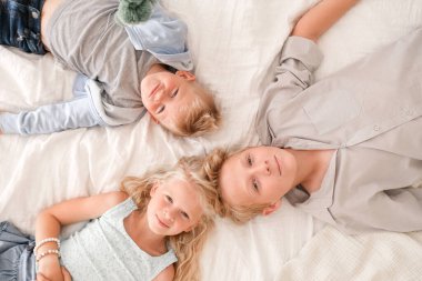 Üç neşeli sarışın çocuk yatakta birlikte yatıyor, kameraya bakıyor ve gülümsüyorlar. İki erkek ve kız. Mutlu aile, erkek ve kız kardeş