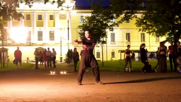 Artista callejero con palos brillantes llameantes para los turistas, gira la llama en la oscuridad al aire libre. espectáculo de incendios. Atractivo concepto de entretenimiento profesional. Rusia San Petersburgo 27.08.19 — Vídeo de stock