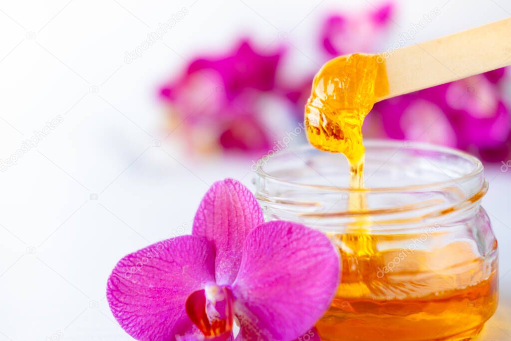 sugar paste or wax honey for hair removing flows down from wooden waxing spatula sticks. flower background - depilation and beauty concept
