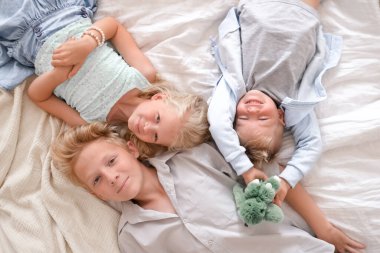 Üç neşeli sarışın çocuk yatakta birlikte yatıyor, kameraya bakıyor ve gülümsüyorlar. İki erkek ve kız. Mutlu aile, erkek ve kız kardeş