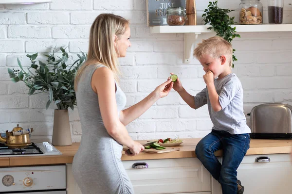 Blonde family mother and son eating healthy food in kitchen at home, green salad on plates — Stock Photo, Image